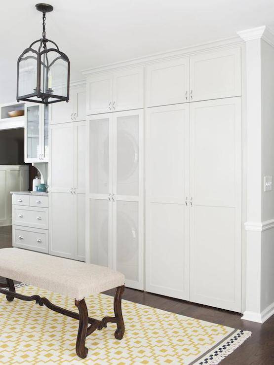 Gorgeous kitchen with ceiling height pantry cabinets flanking a hidden stacked washer and dryer concealed behind mesh front doors. The multi functional room features an arch top lantern pendant, hung above a linen bench atop an Ikea Alvine Ruta Rug.