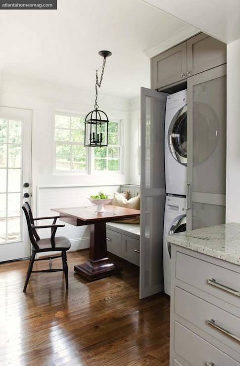 TerraCotta Properties - Laundry room in kitchen with white stacked front loading washer & dryer enclosed in mesh doors, gray cabinets painted Sherwin Williams Pavestone, granite countertops, built-in banqueete painted gray Sherwin Williams Pavestone, square pedestal dining table and iron lantern.