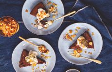 Chocolate torte with Baileys cream and salted praline on white plates with gold forks