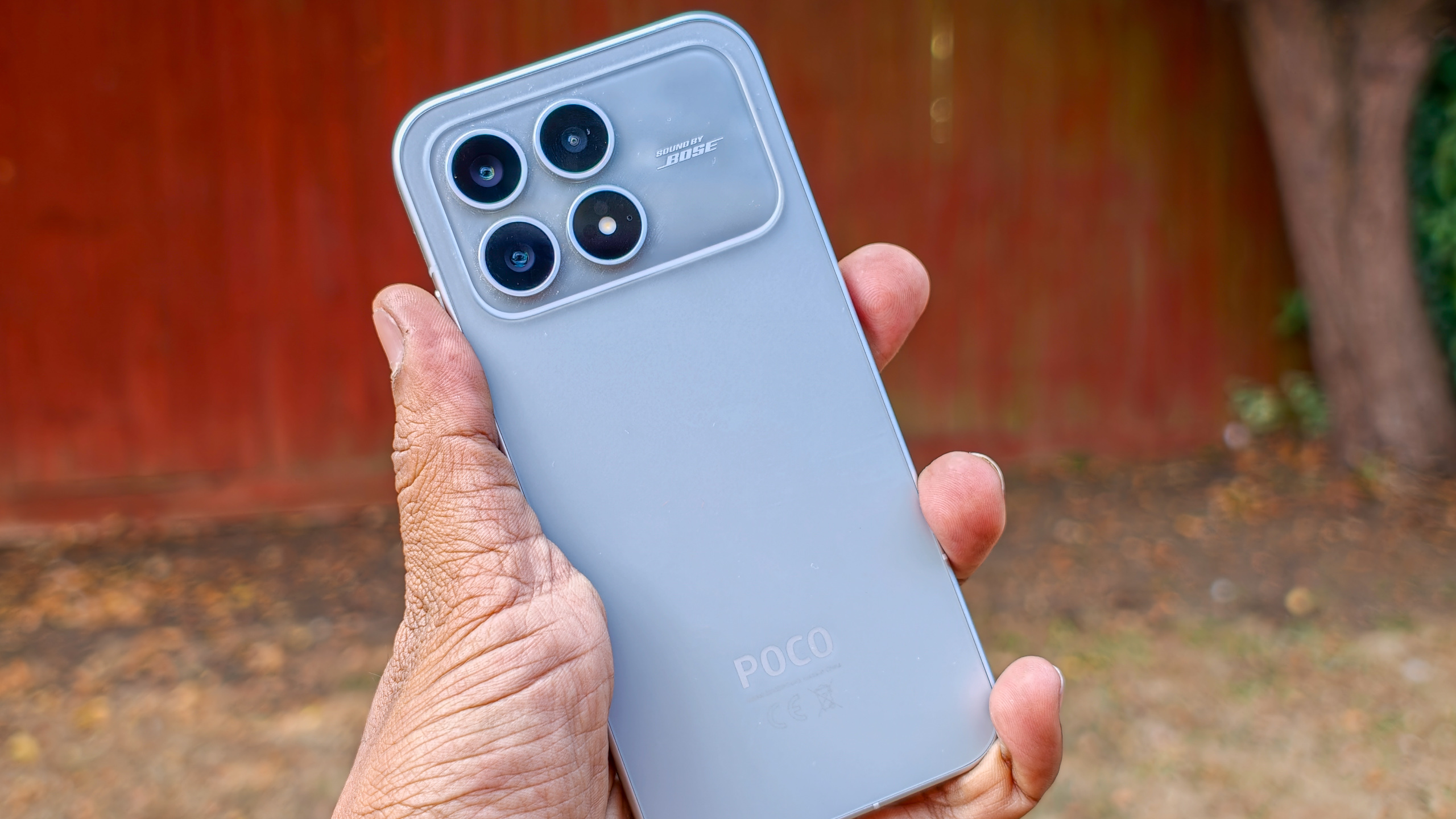 The Poco F8 Pro in Silver in the hand against a garden backdrop