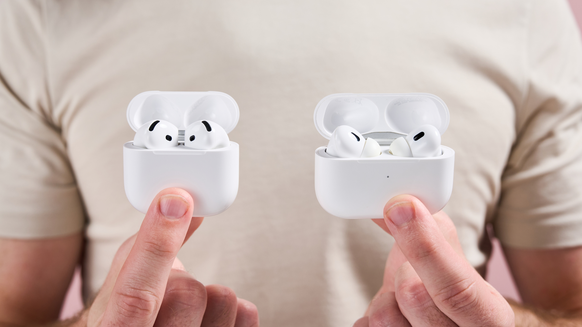 &Aring;pne etuier til AirPods Pro 2 og AirPods 4 holdes ved siden av hverandre, og viser toppen av &oslash;reproppene som stikker ut