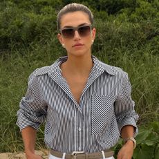 Cass Dimicco wears a striped button-down shirt, tan belt, white jeans, and sunglasses.