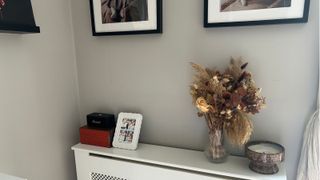 Corner of living room with radiator shelf, frames on wall and dried flower bouquet