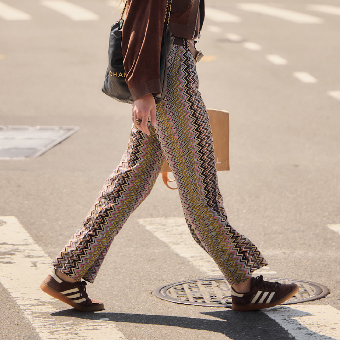 woman walking the street wearing zig-zag printed pants and brown adidas sneakers