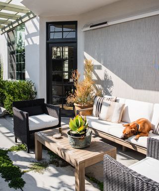 A shaded patio area with black rattan chairs and a wooden table with a plant on it