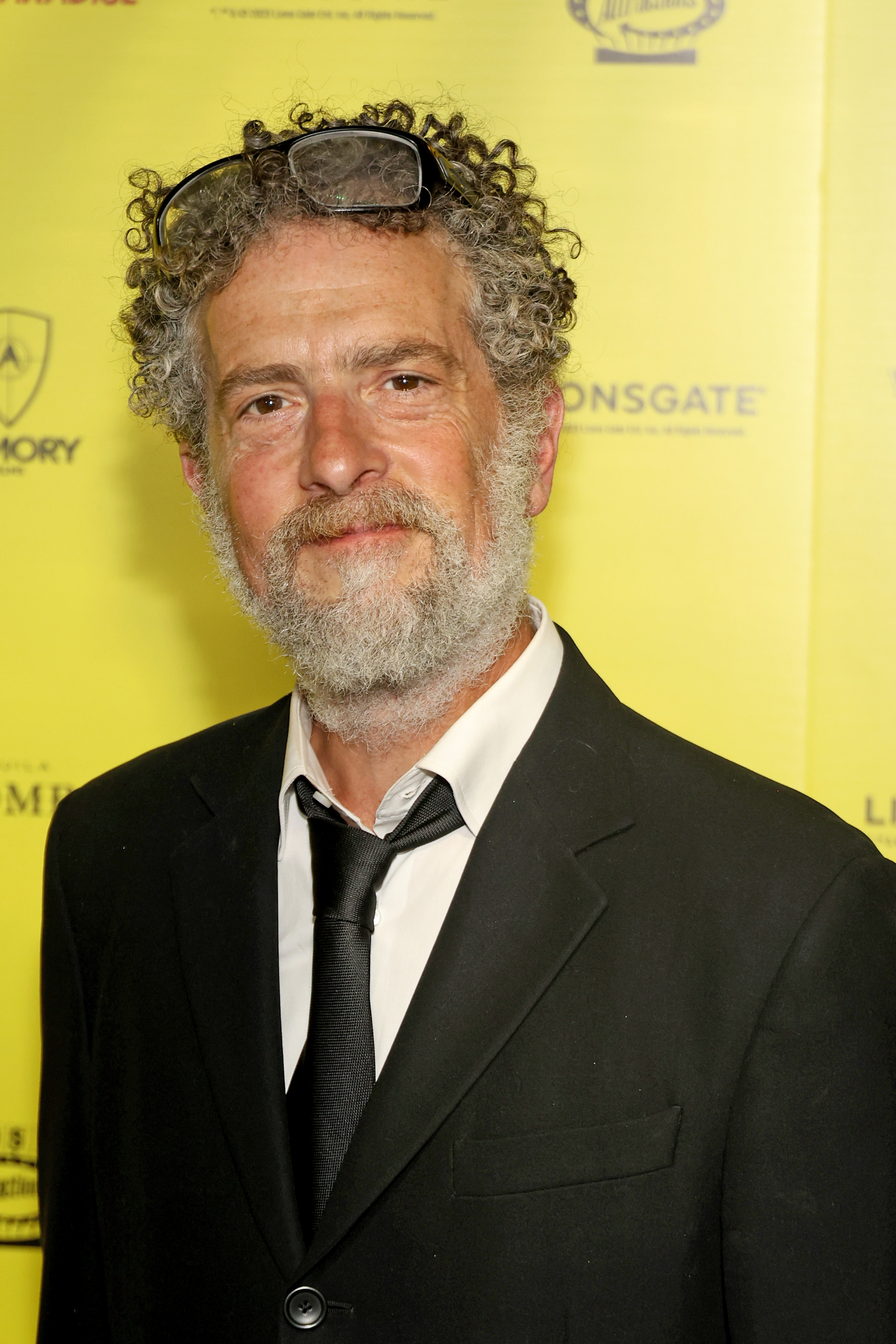 actor john ales wears a black suit and poses on a red carpet