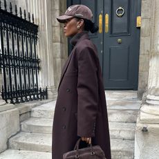 Marilyn wears a brown baseball cap, brown coat, brown patrizia bag, and jeans.