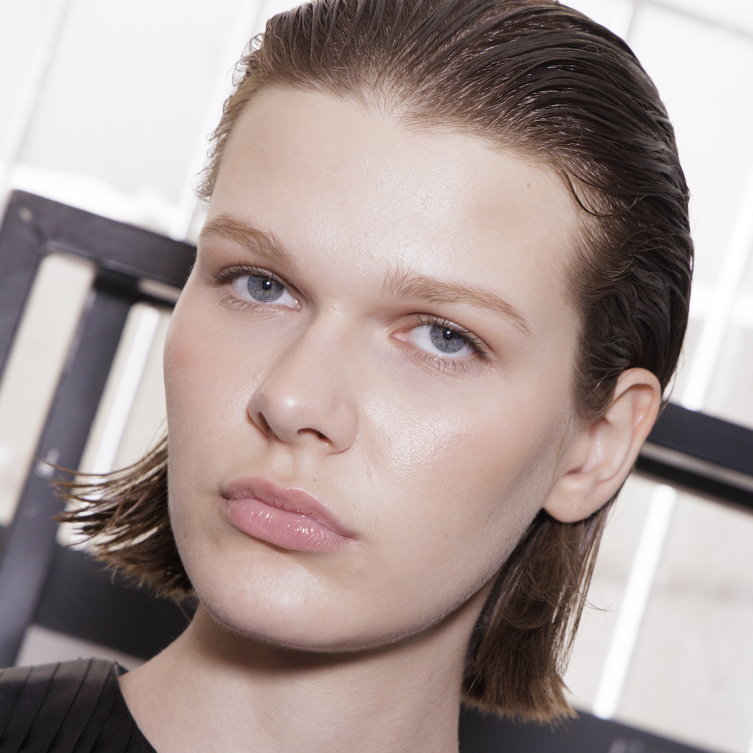 Model with bright dewy skin and slicked back hair backstage at fashion week