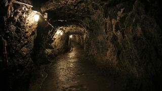 Interior of a mine. We see a dark tunnel lit at regular intervals by electric lamps.