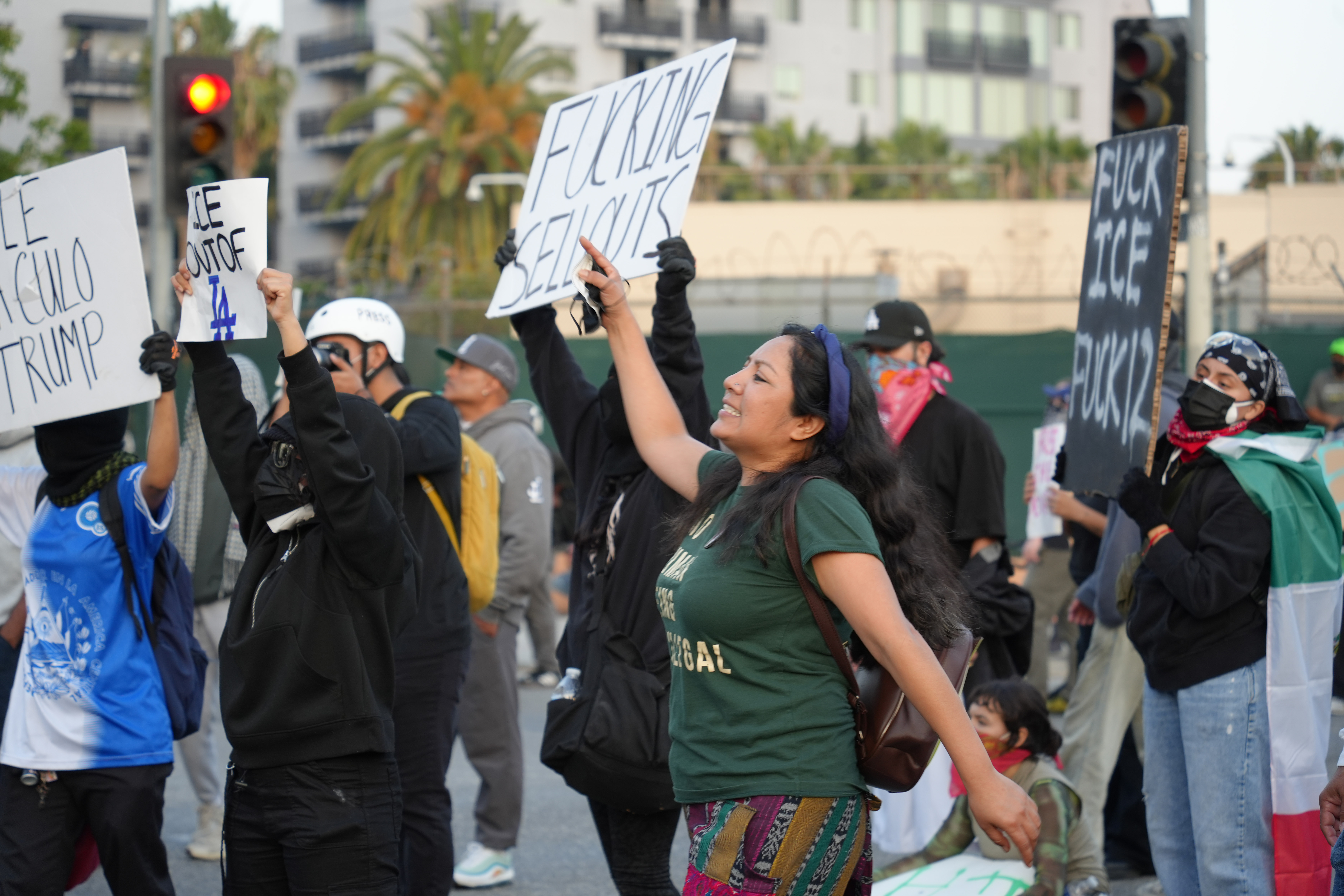 A woman in green raises her sign with one hand while marching.
