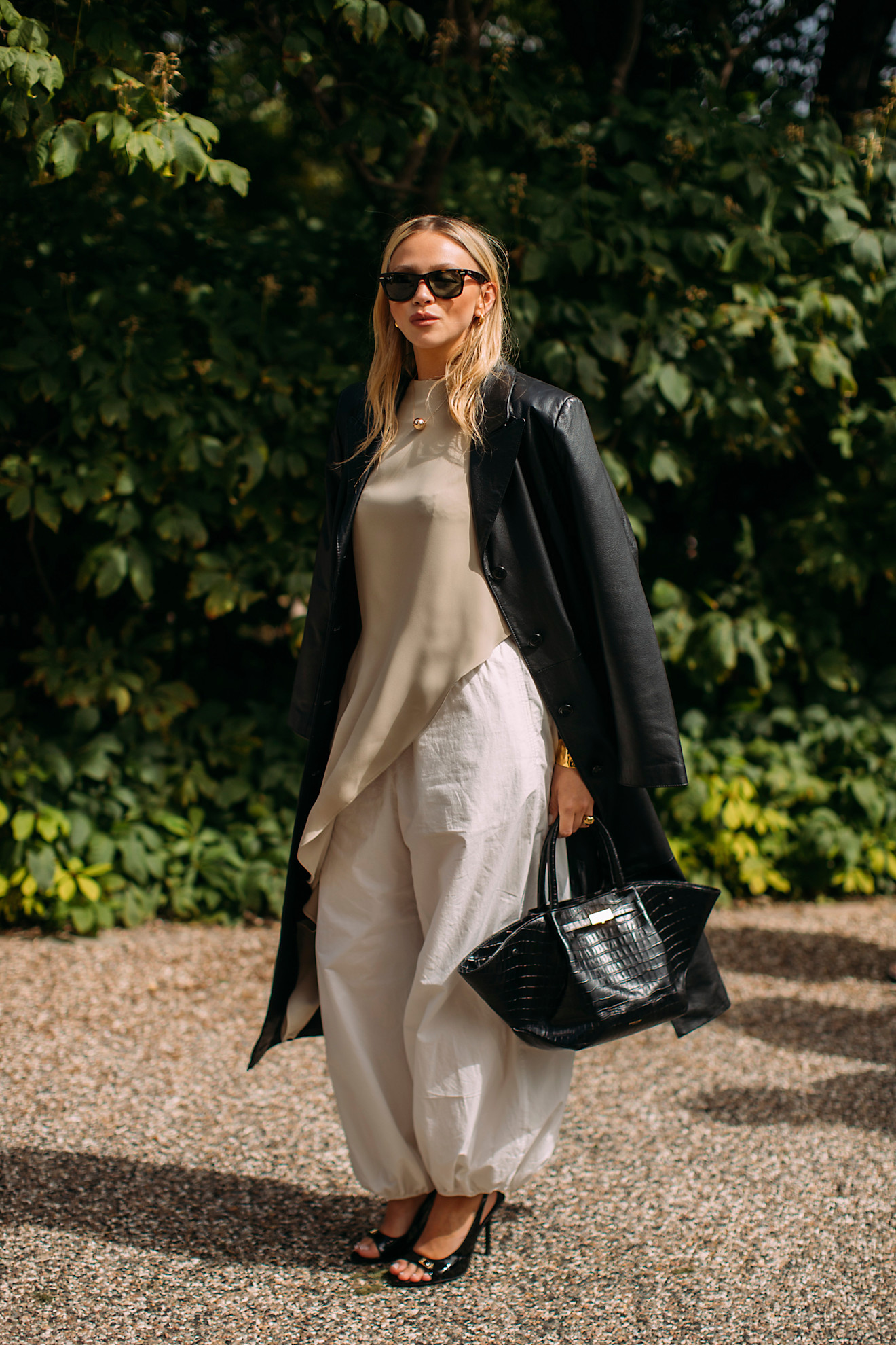 fashion week attendee wearing sunglasses, leather jacket, billowing white pants, and peep toe heels