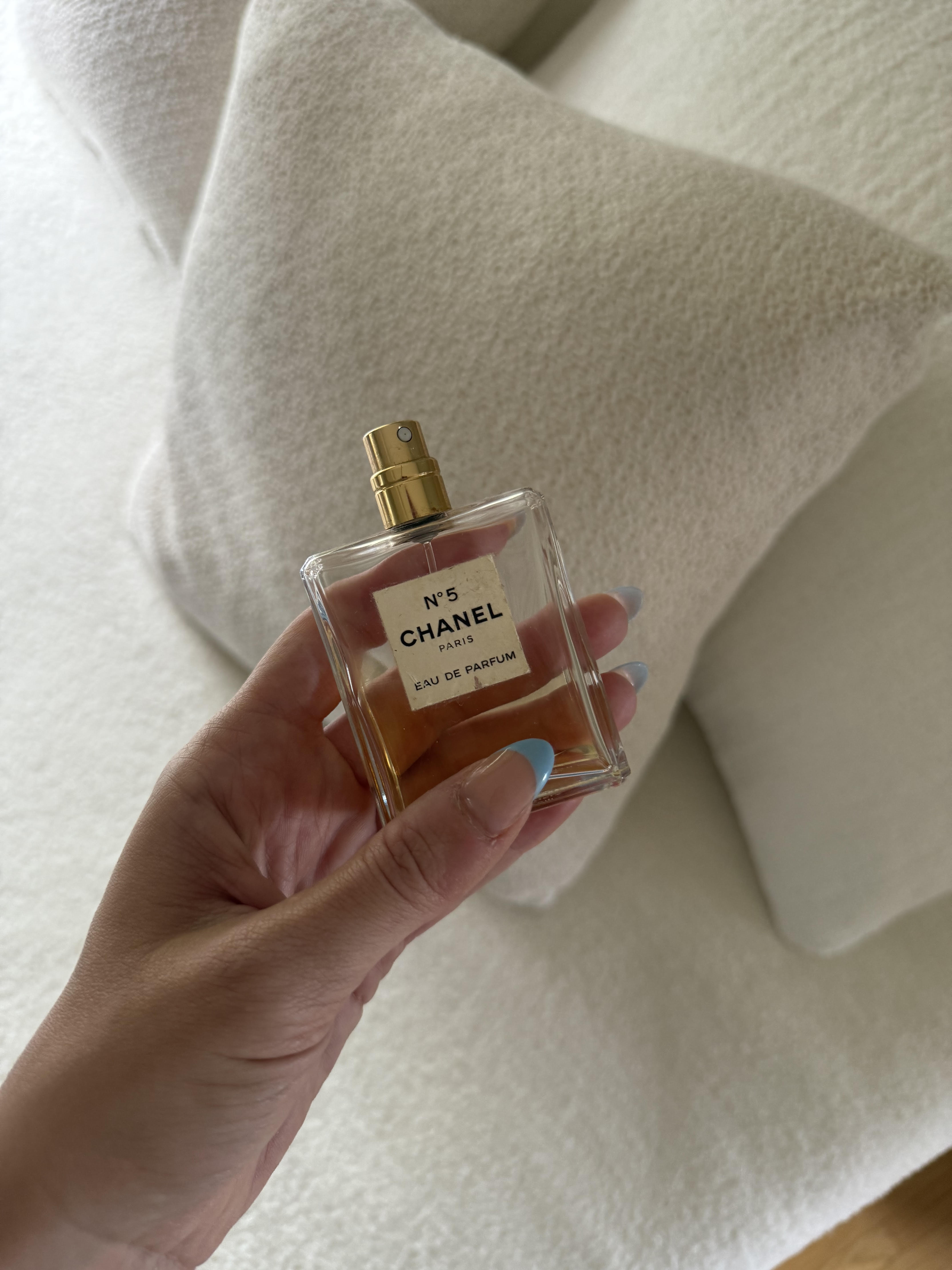 a woman&#039;s hand holding a glass bottle of Chanel No.5 perfume