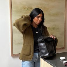 @monikh wearing a green Khaite sculpted cashmere cardigan with jeans and a black tote bag.