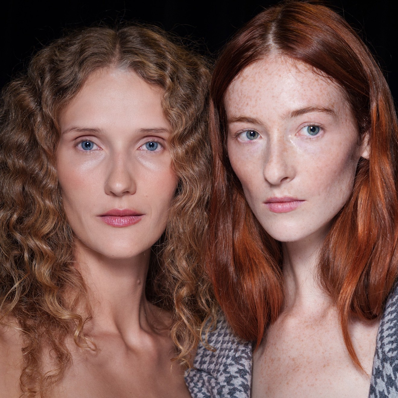 two pale models with blonde and red hair on a black background
