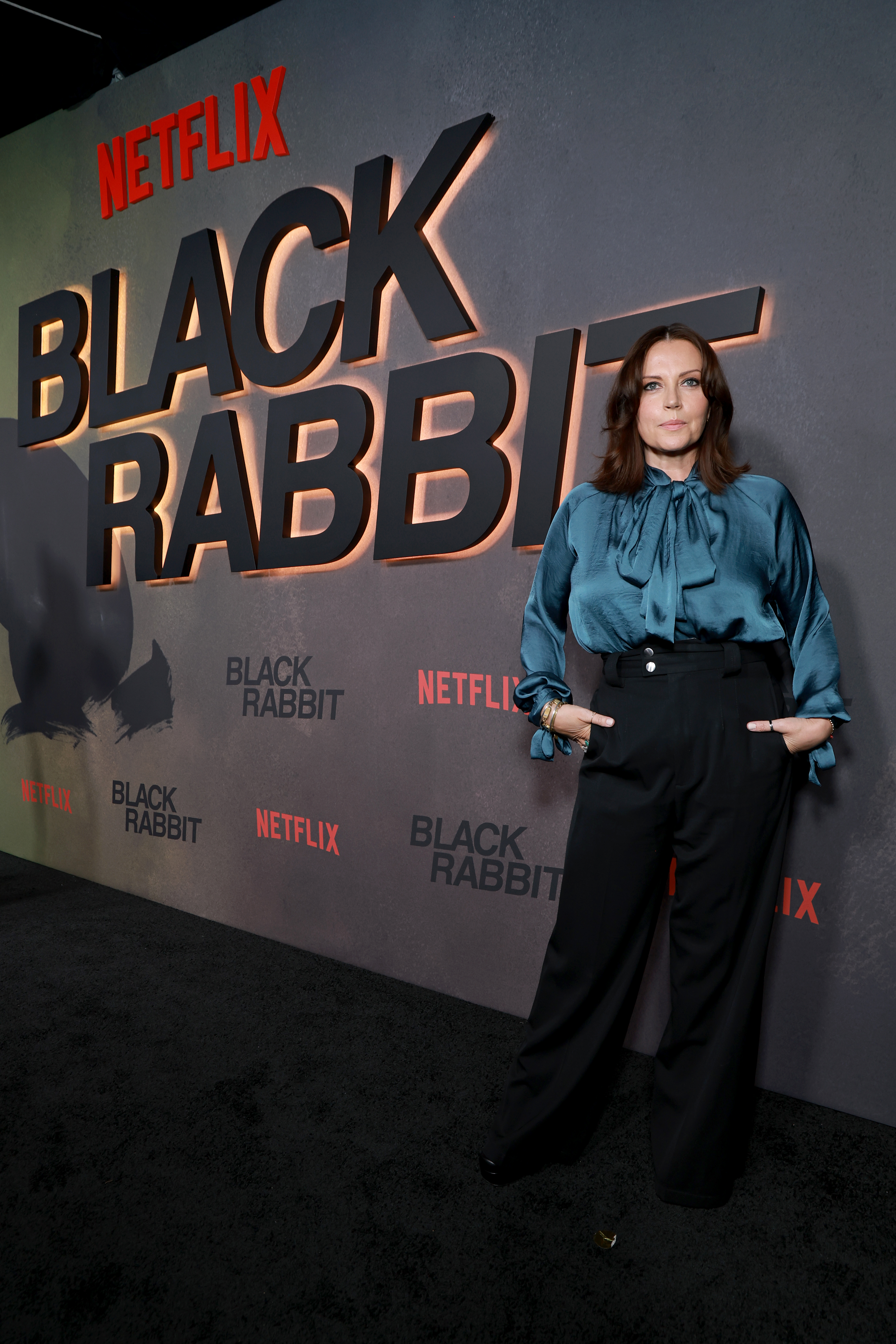 Dagmara Domińczyk wears a blue blouse and black pants posing on a red carpet at the black rabbit premiere