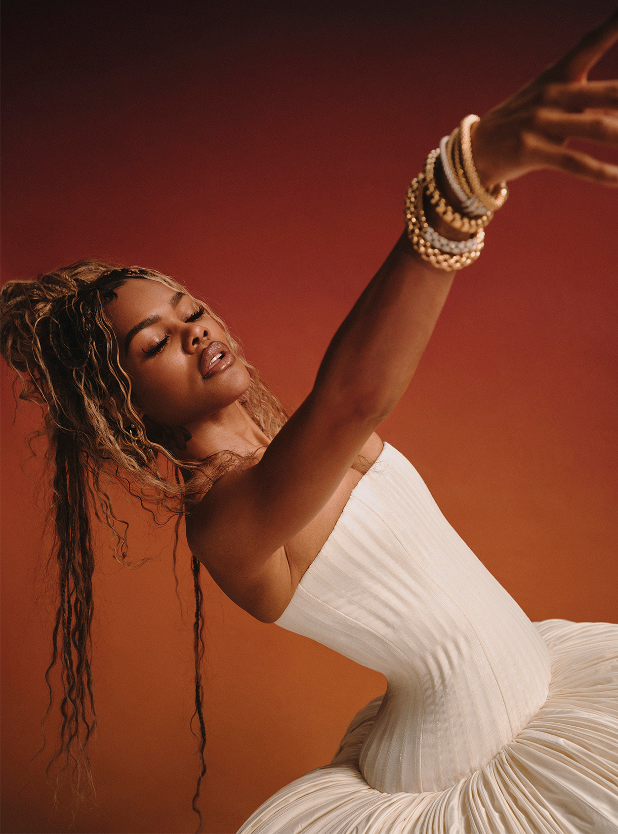Teyana Taylor reaching for the camera wearing silver and gold bangles and an ivory puff dress