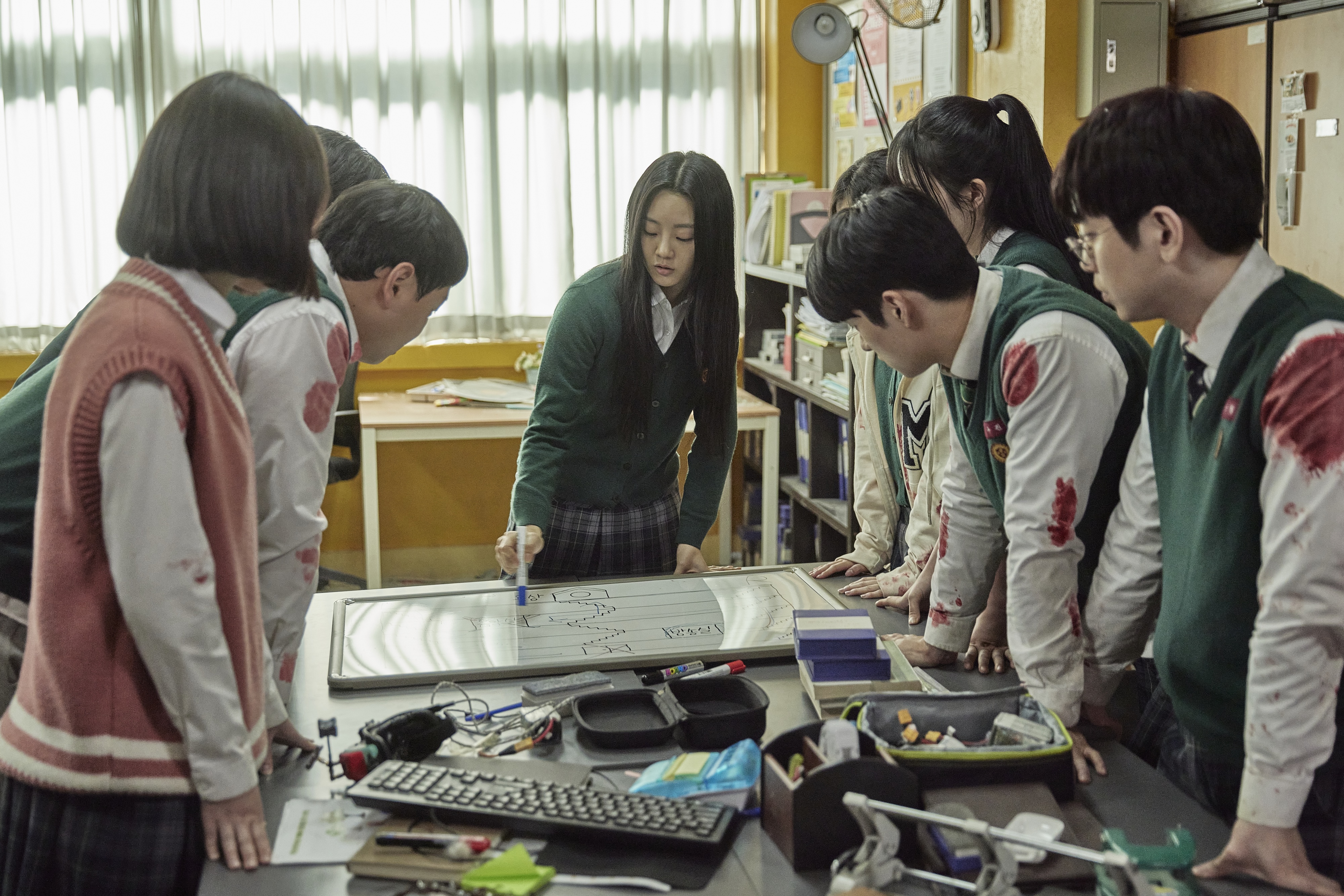 A girl (Cho Yi-hyun as Choi Nam-ra, center) draws a plan for a group of students, in &#039;All of Us Are Dead.&#039;