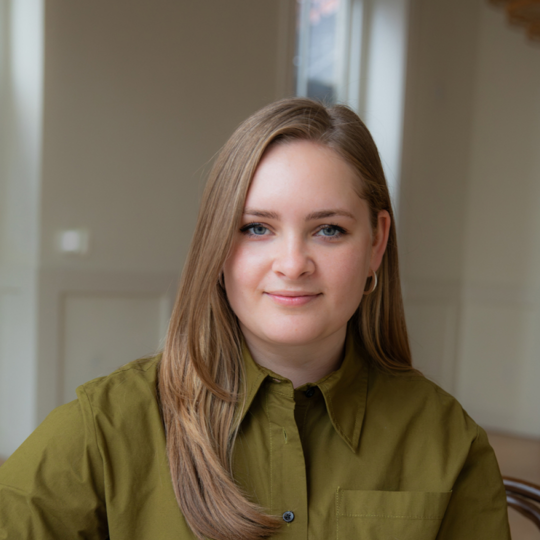 A photo of Lisa Vedernikova Khanna, wearing a button-up olive-green shirt, smiling in an indoor setting.