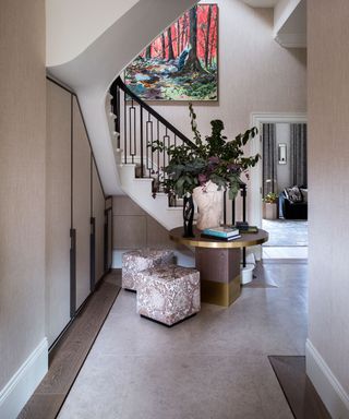 Narrow hallway ideas shown in a beige scheme with round gilt-edged table and square footstools.