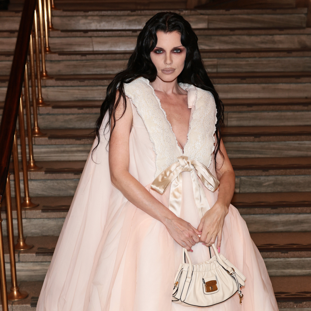 Julia Fox posing in front of steps wearing a frilly dress, dramatic eye makeup and black hair.