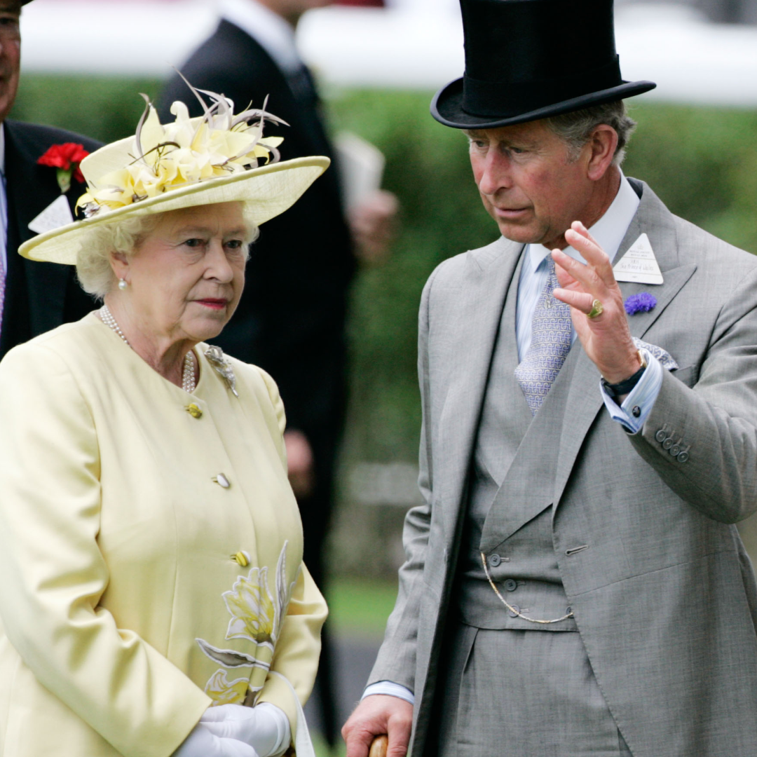 Queen Elizabeth II wears a pale yellow outfit while her son King Charles waves in front of her face, and Queen Camilla stands to the side ignored wearing white