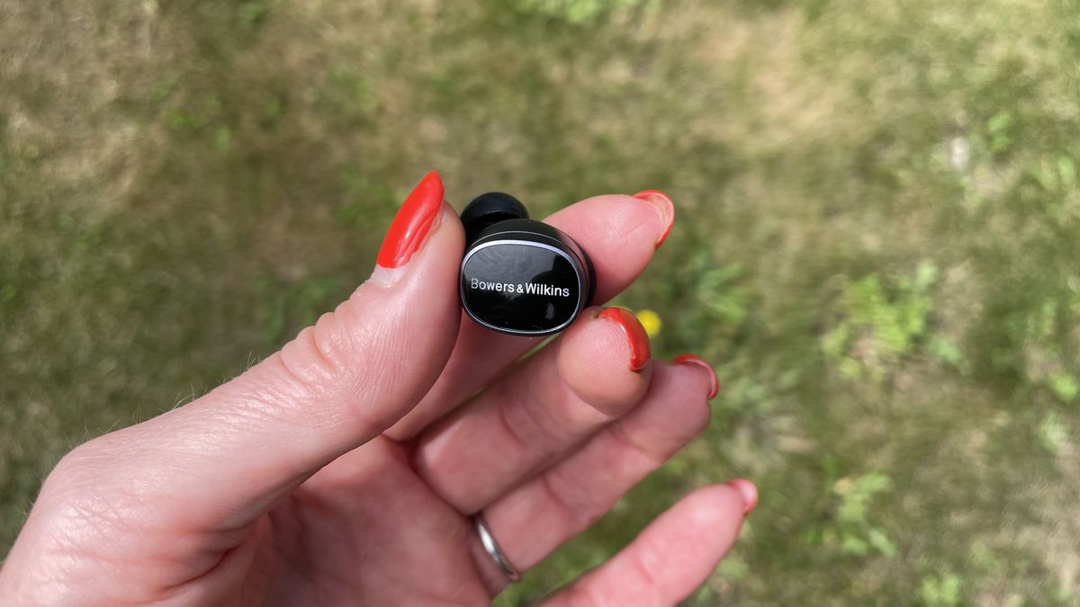 Bowers &amp; Wilkins Pi8 earbuds, held in a hand on grassy background