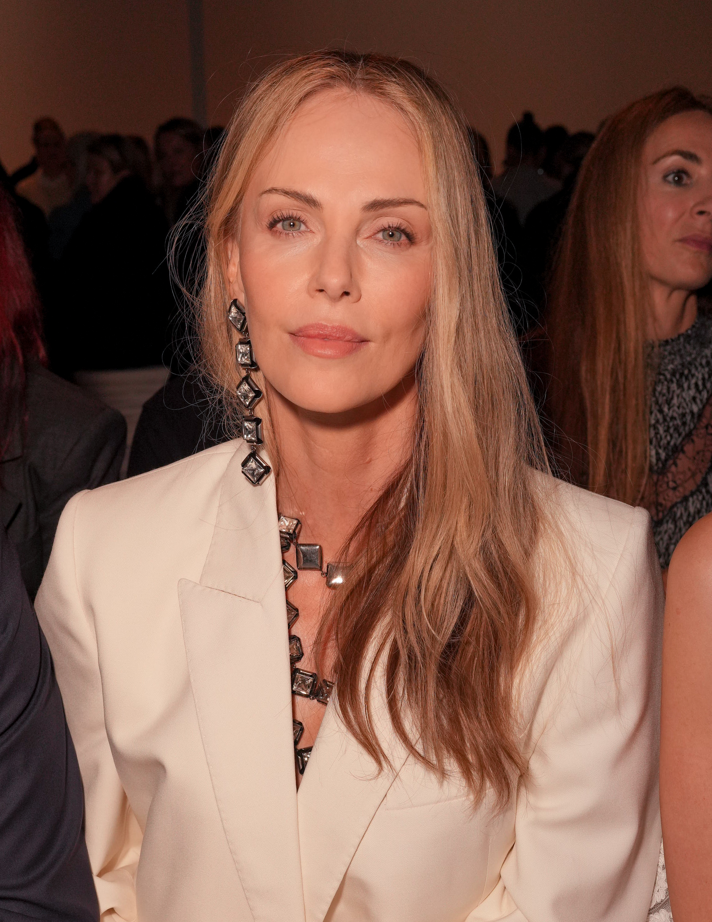 a white woman with blonde hair pictured sitting at a fashion show wearing a white suit