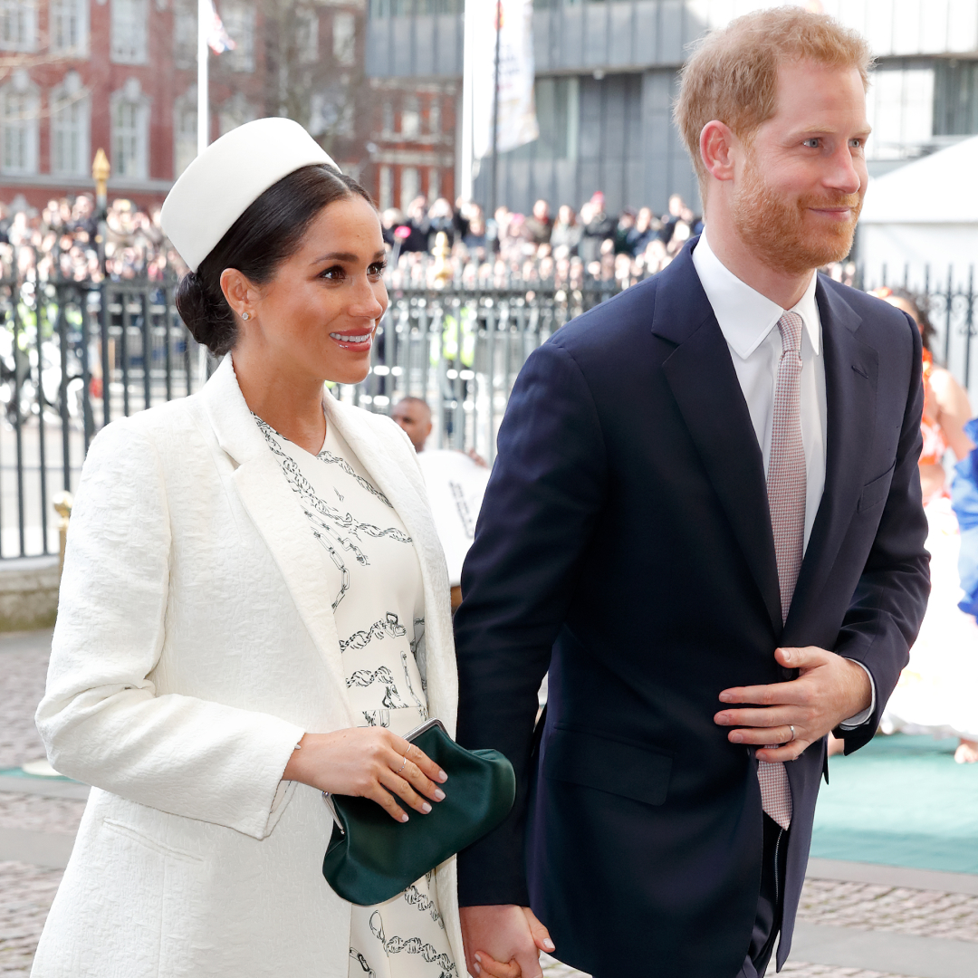 Meghan Markle wearing a white hat and coat holding hands with Prince Harry at Westminster abbey