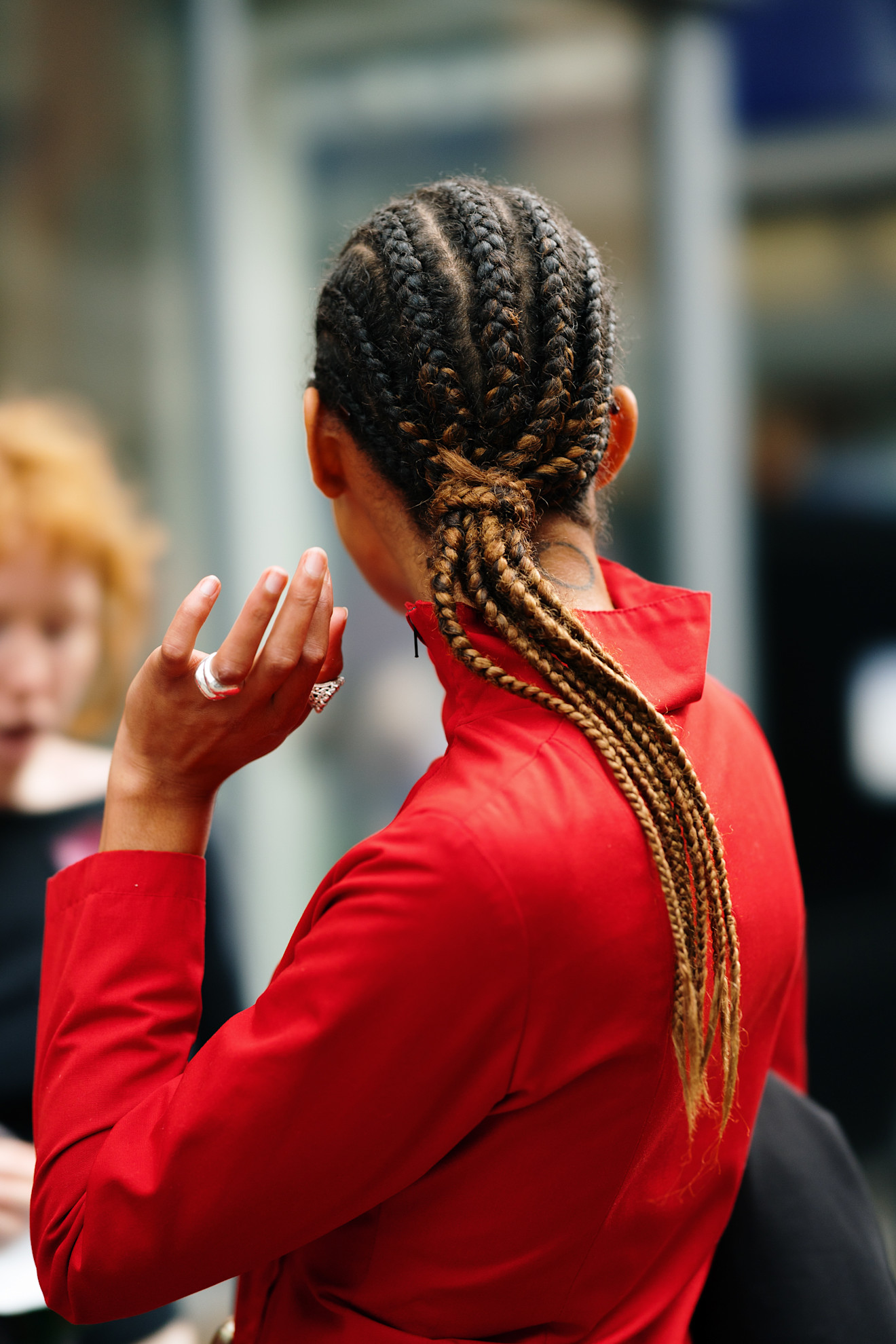 a woman in a red shirt from the back with a cornrow ponytail and silver rings on her left hand
