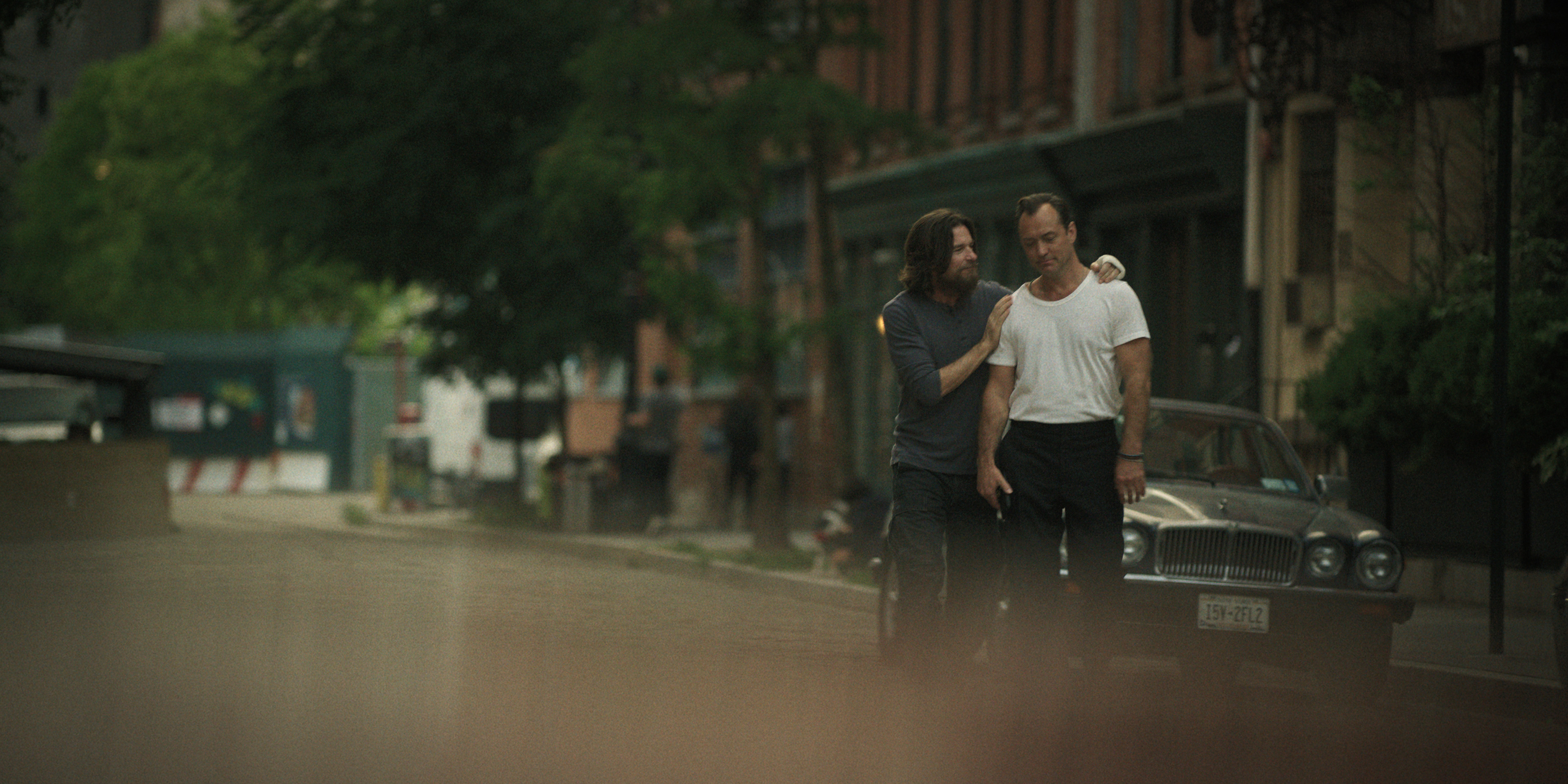 jason bateman and jude law embracing while walking through the street in black rabbit