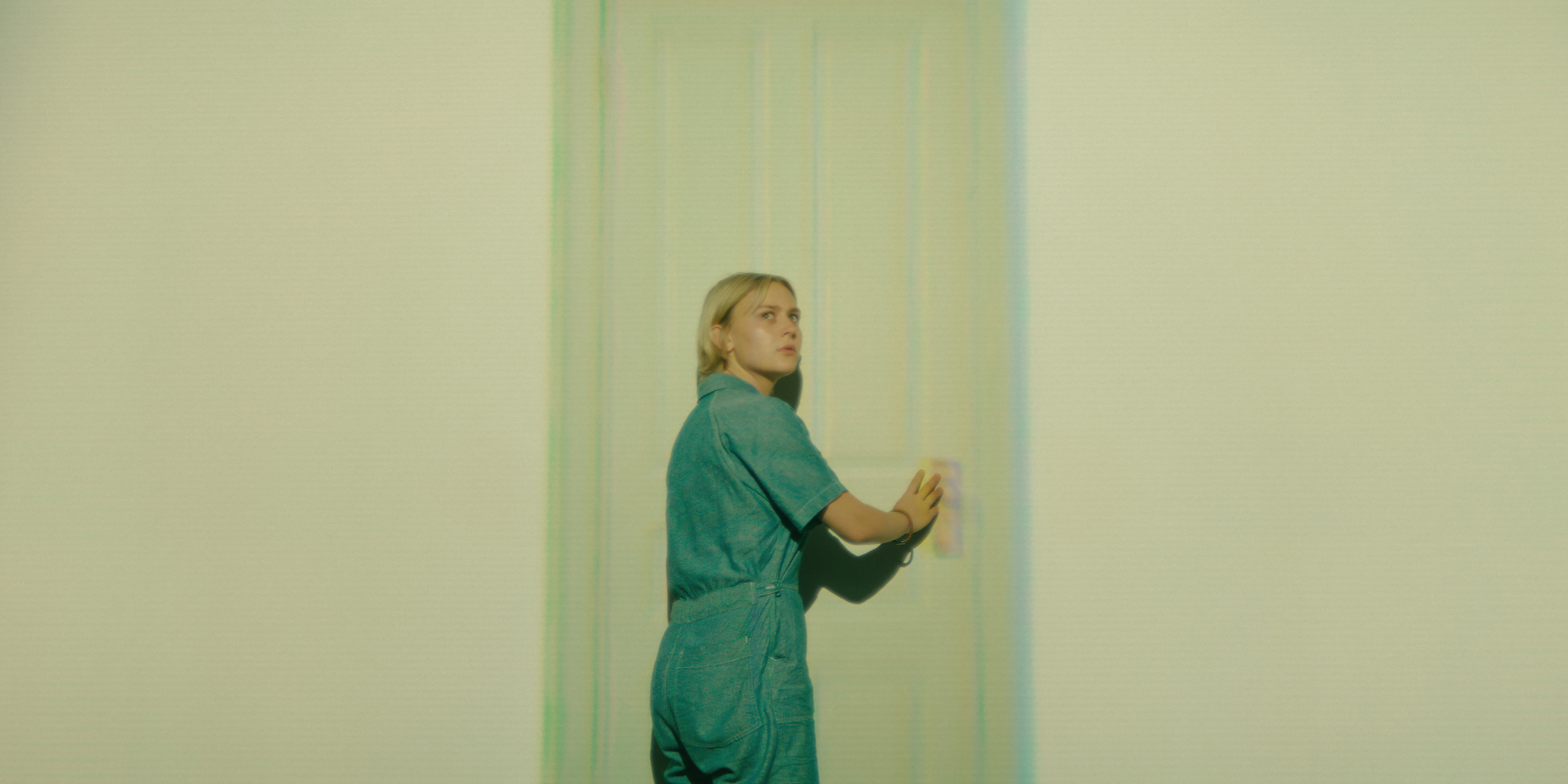 Alyvia Alyn Lind as Leila wearing a blue jump suit in a weird room with a light projecting a door in wayward