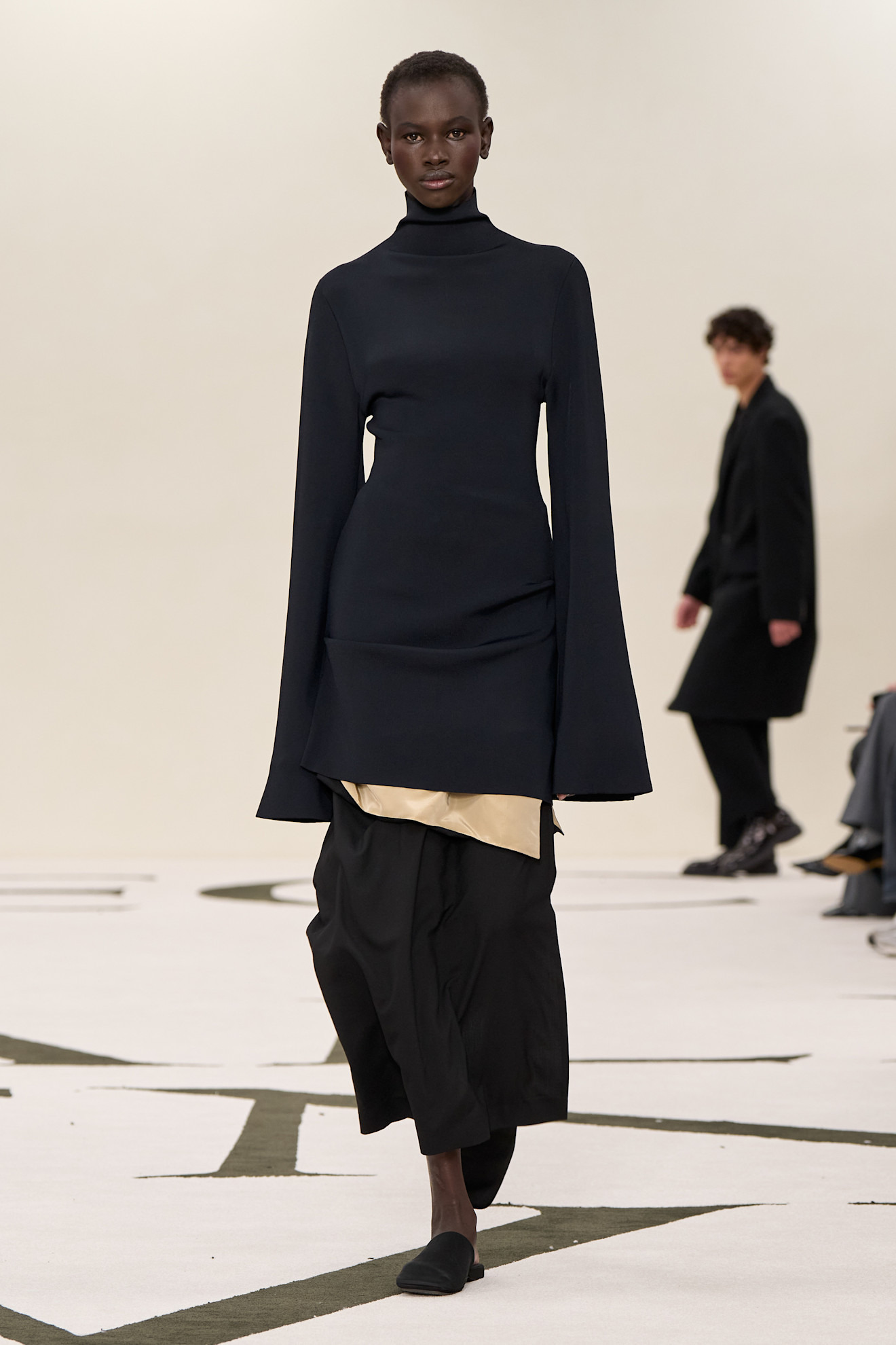a model at Calvin Klein Fall 2025 wearing black slippers, black dress, and black skirt