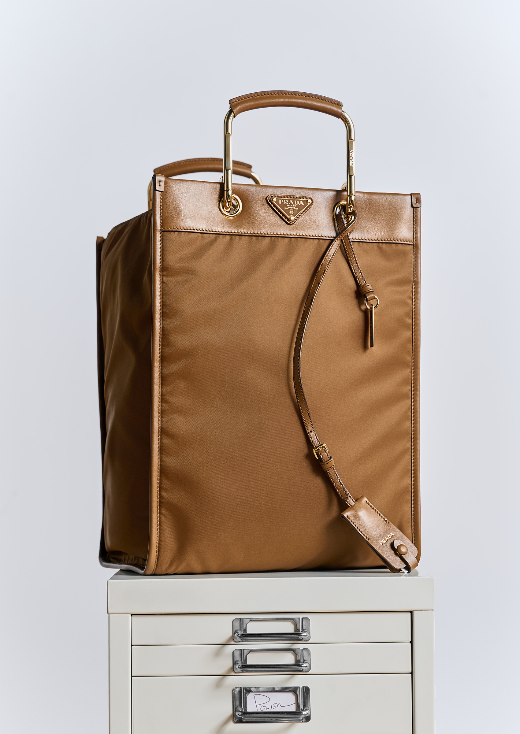 A brown Prada tote bag on top of a white file cabinet.