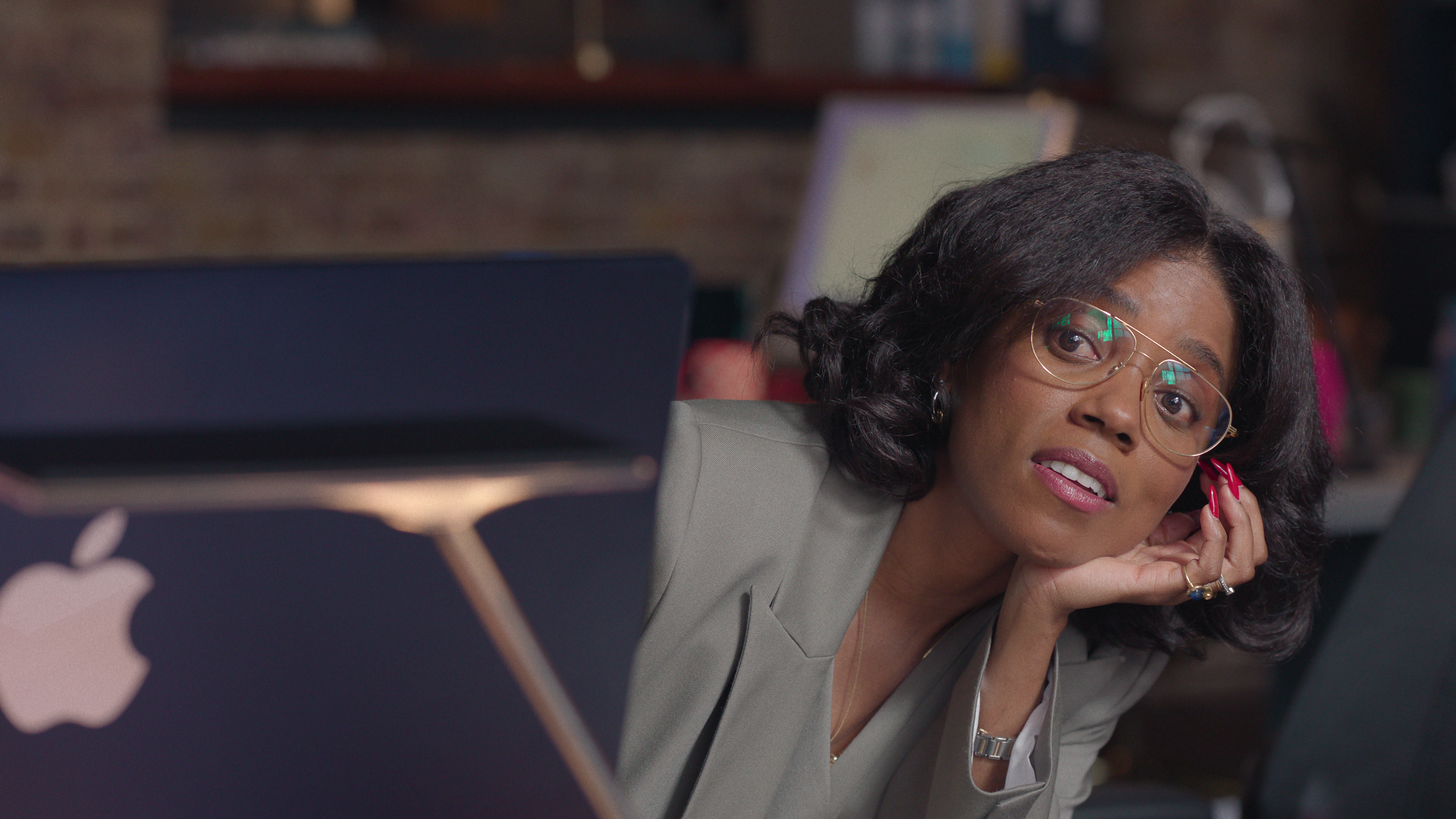 janicza bravo as kim looking around her laptop at her desk in too much