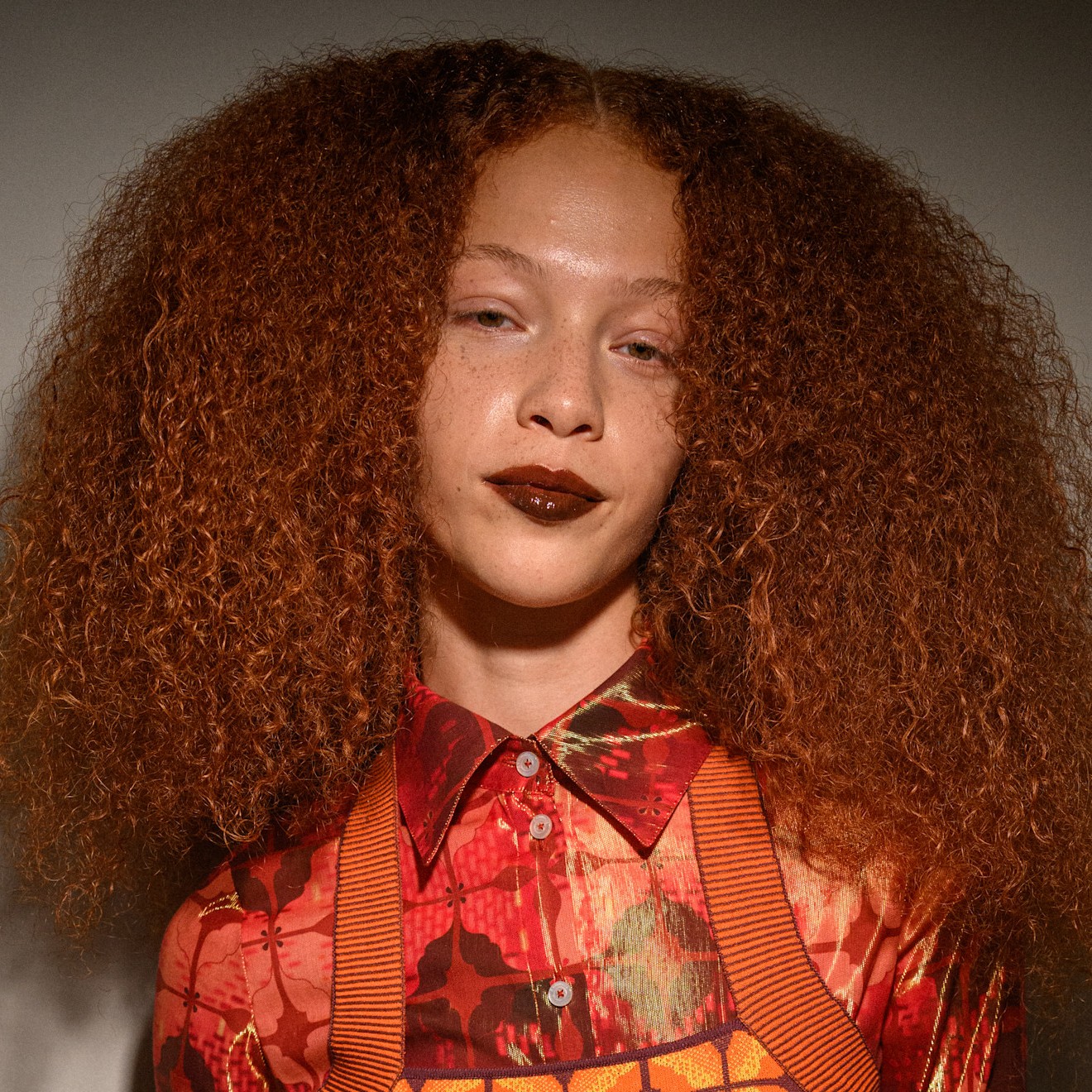 women with red curly hair in a red and orange shirt smiling at the camera