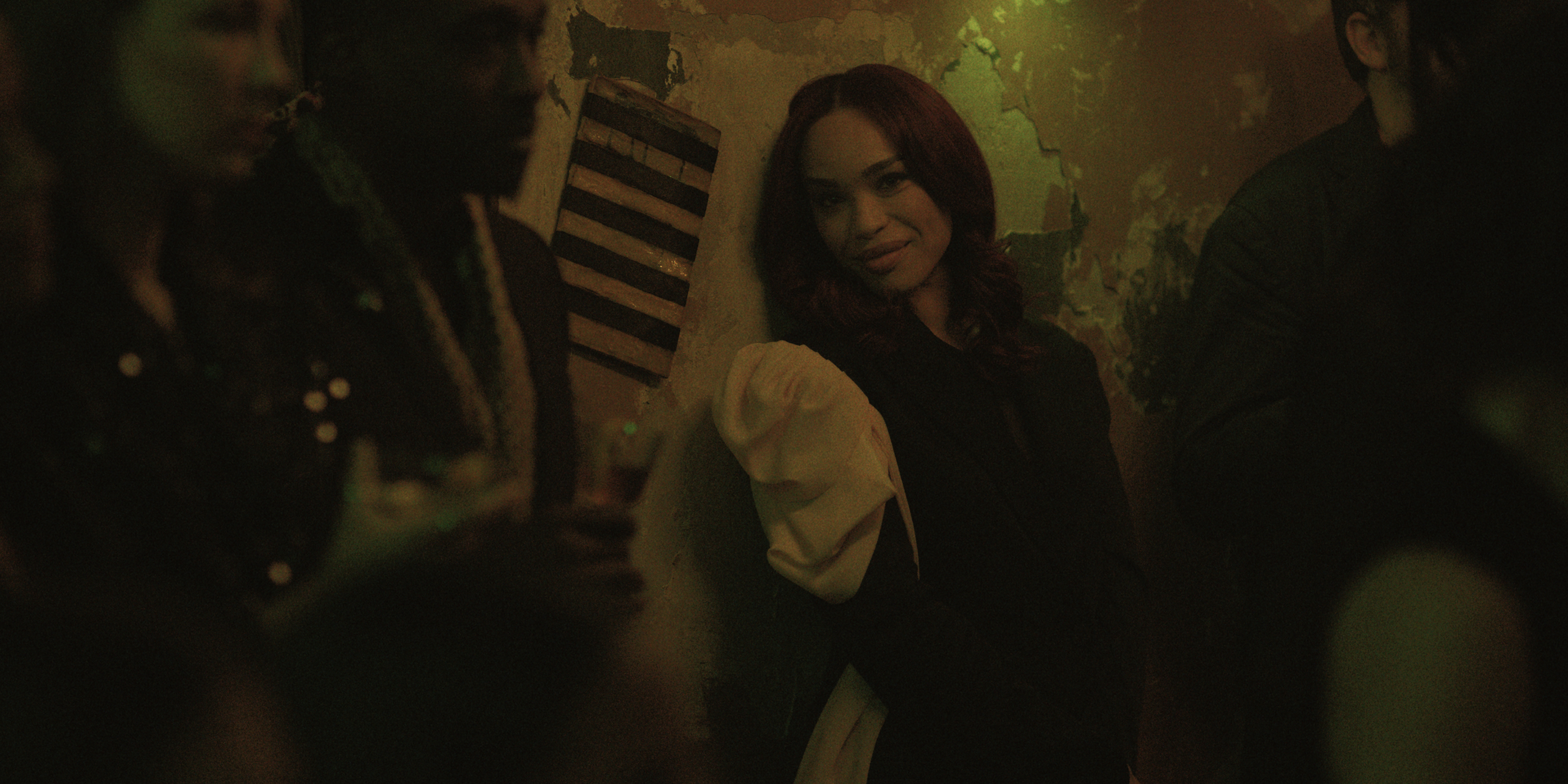 cleopatra coleman as estelle smiling and leaning next to the wall in a club in black rabbit