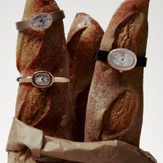 Photos of Cartier Baignoire watches on baguettes inside of a brown paper bag.