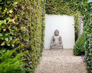 A gravel pathway surrounded by hedges leading to a Buddha statue