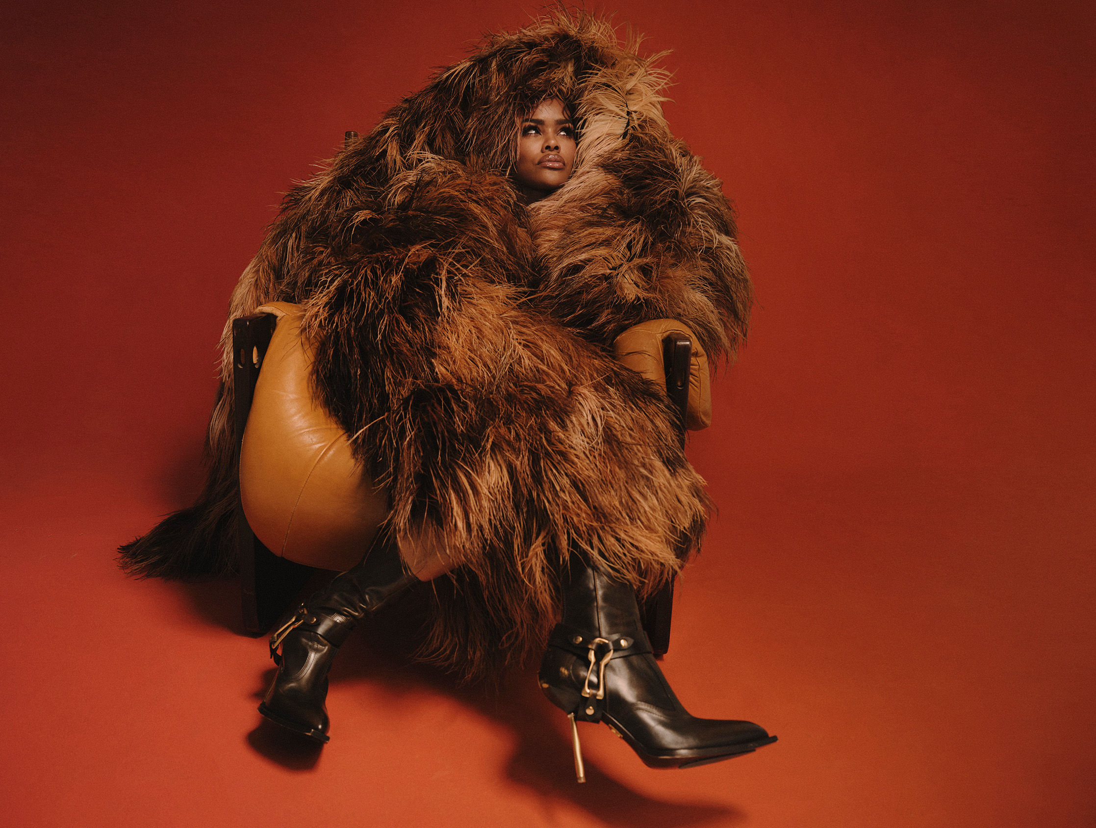 Teyana Taylor wearing a thick fur coat from which only her head is visible, and black heeled boots