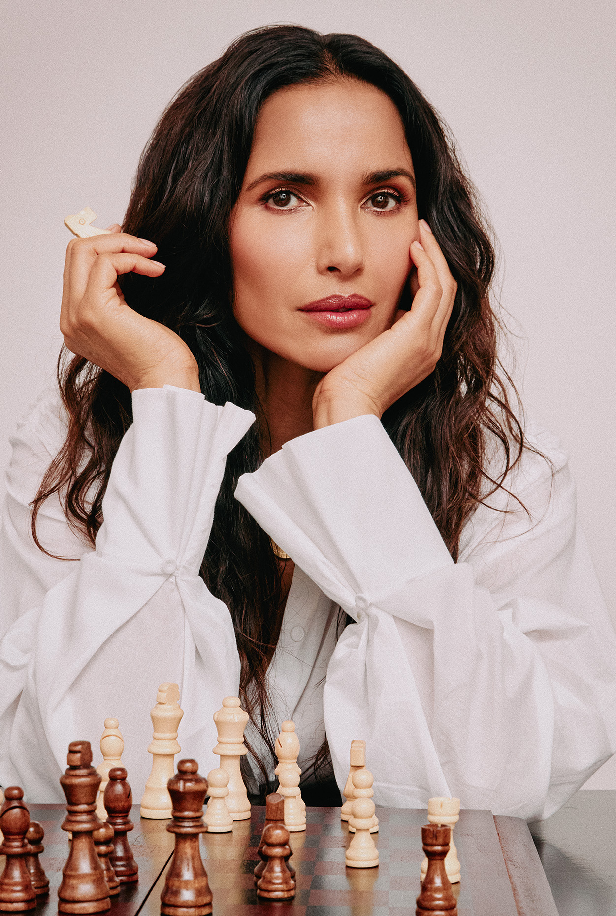 Padma Lakshmi poses in front of a chess board wearing a white blouse