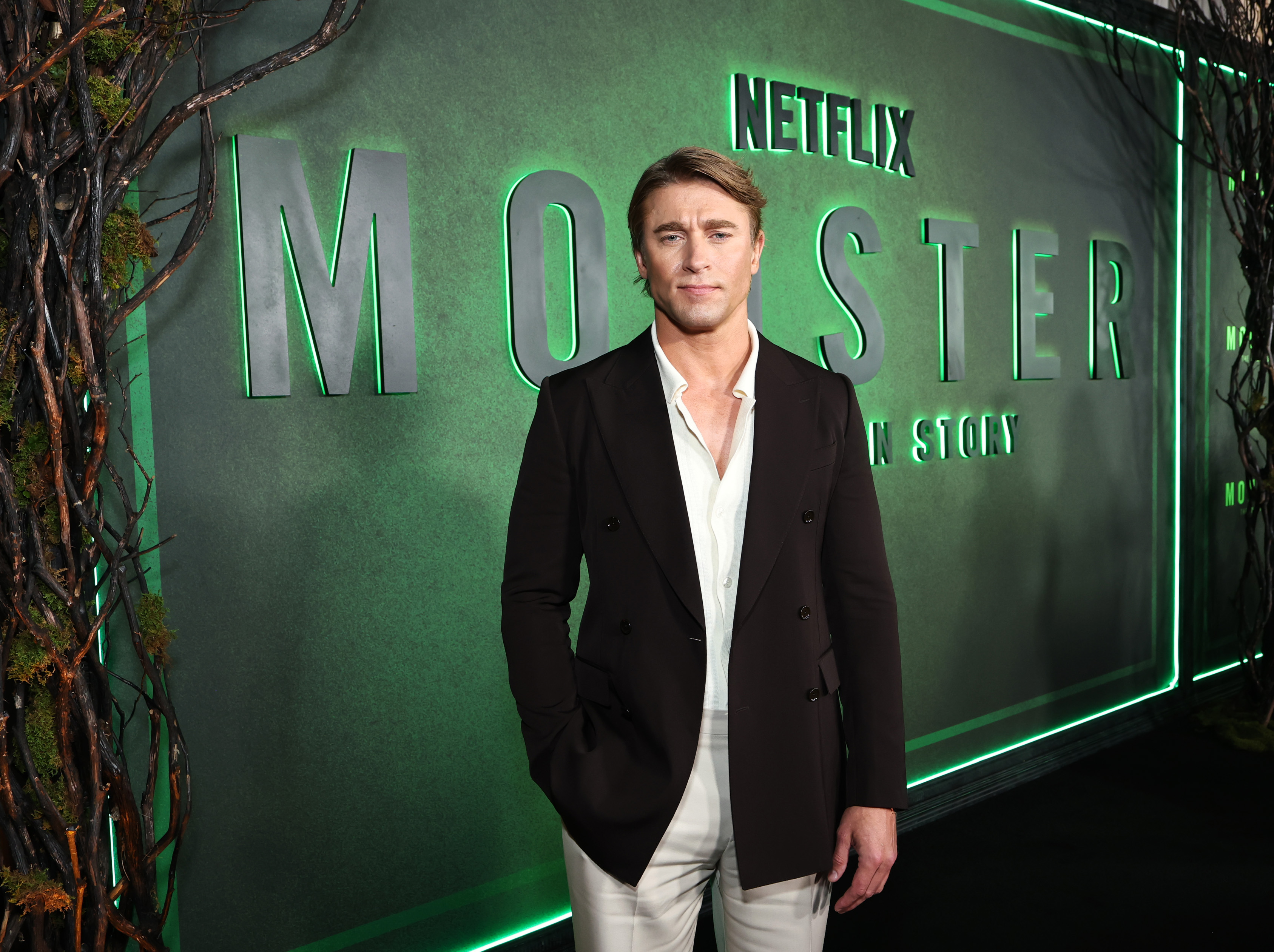 charlie hall wears a black jacket standing on a red carpet for monster the ed gein story