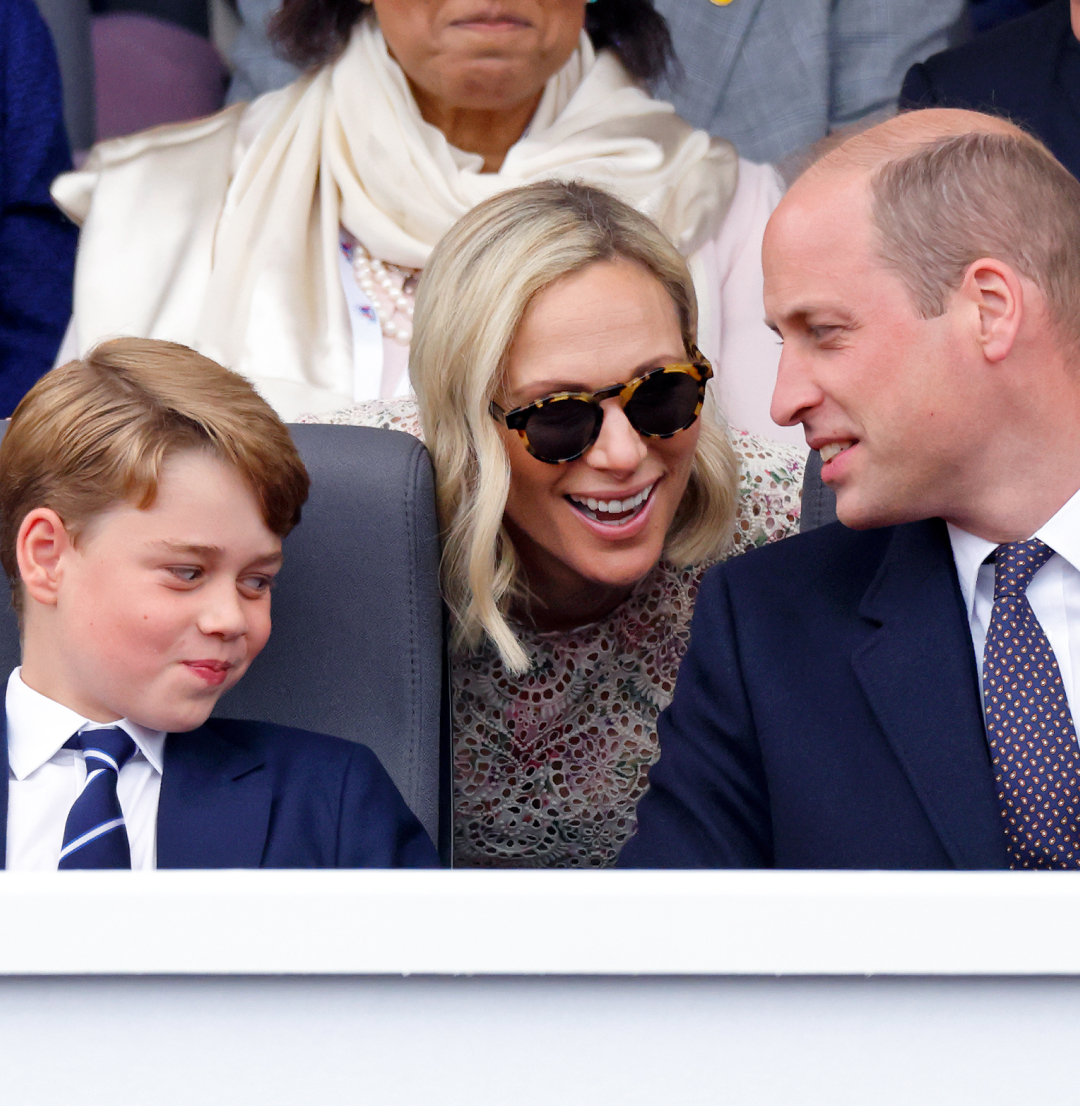 Prince George smirking as Zara Tindall leans over and talks to Prince William