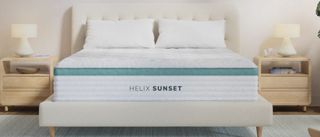 The image shows a white mattress with green trim placed on a taupe colored bed foundation, set within a light and neutral bedroom