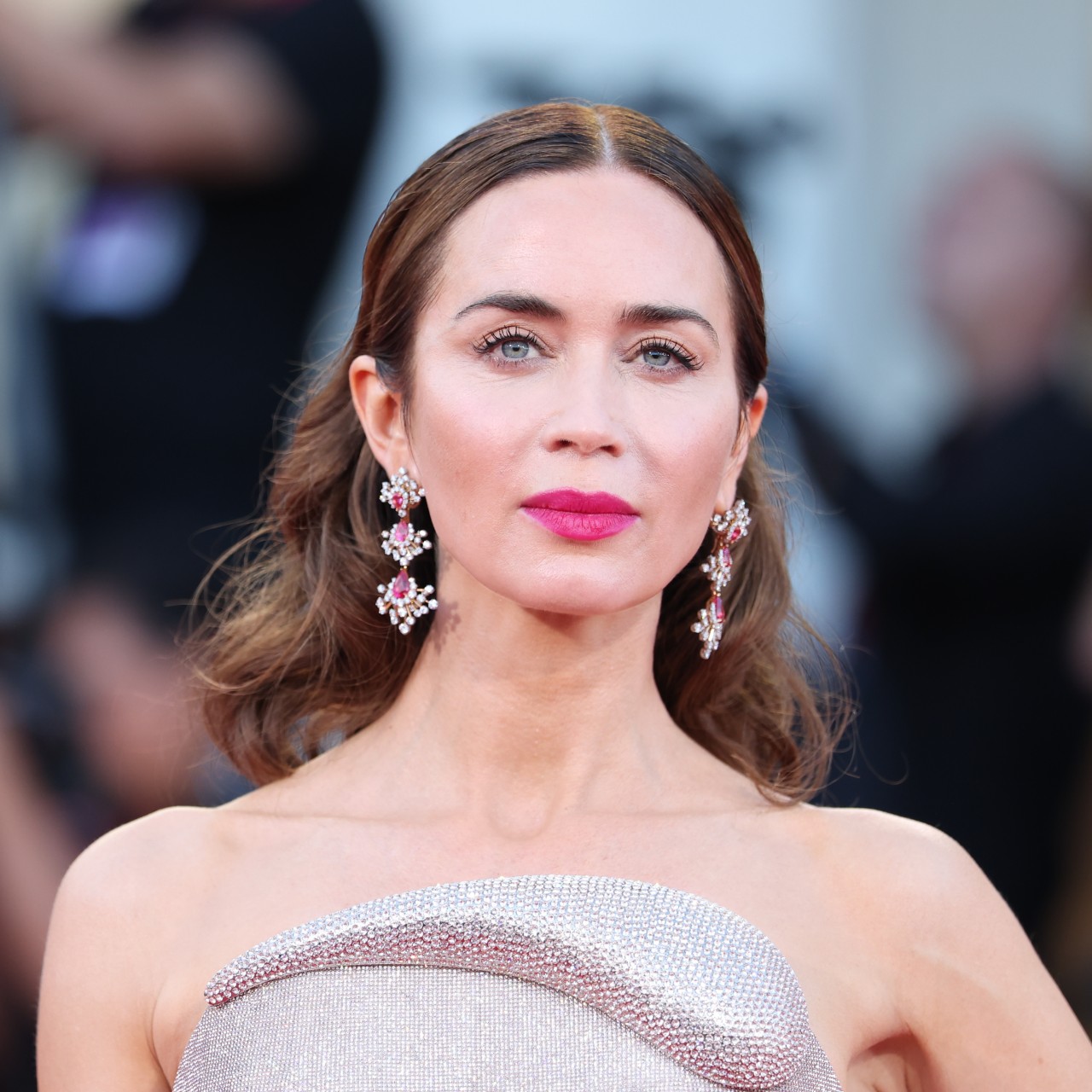 a close up photo of a woman with brown hair wearing red lipstick and posing on a red carpet in front of a crowd of paparazzi