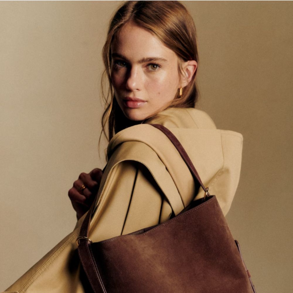 Young woman wearing Sézane trench coat and brown suede bag.