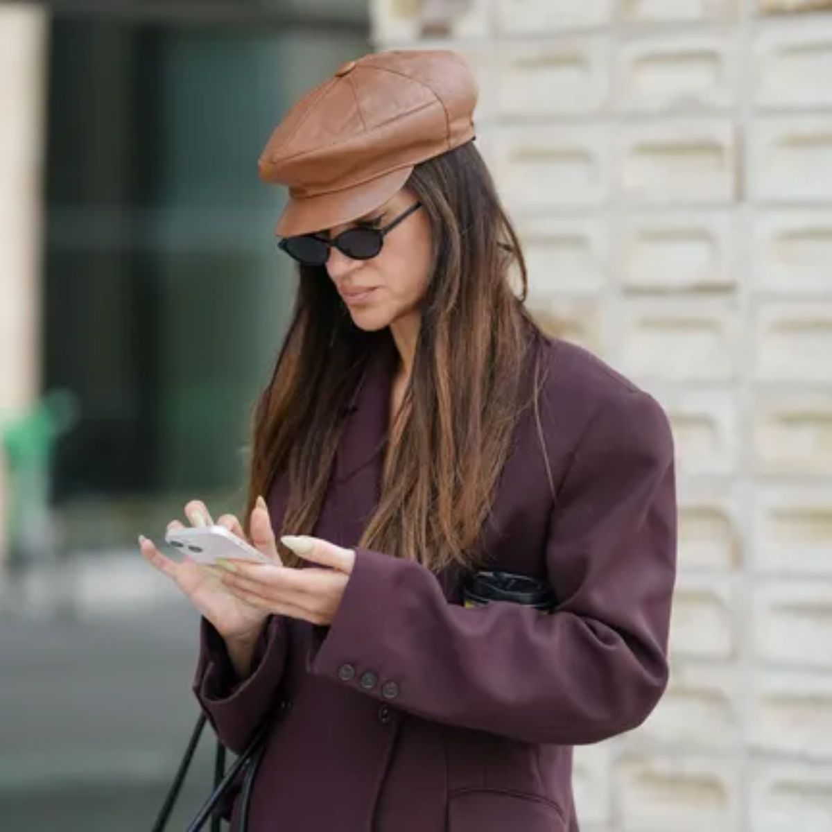 woman wearing a hat, sunglasses and an aubergine-coloured blazer photographed on her phone 