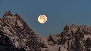 Snowcapped mountains against a clear sky with the moon in the background