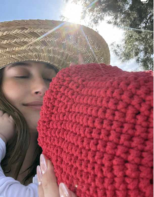 Hailey Bieber holding her son who is wearing a red knit hat
