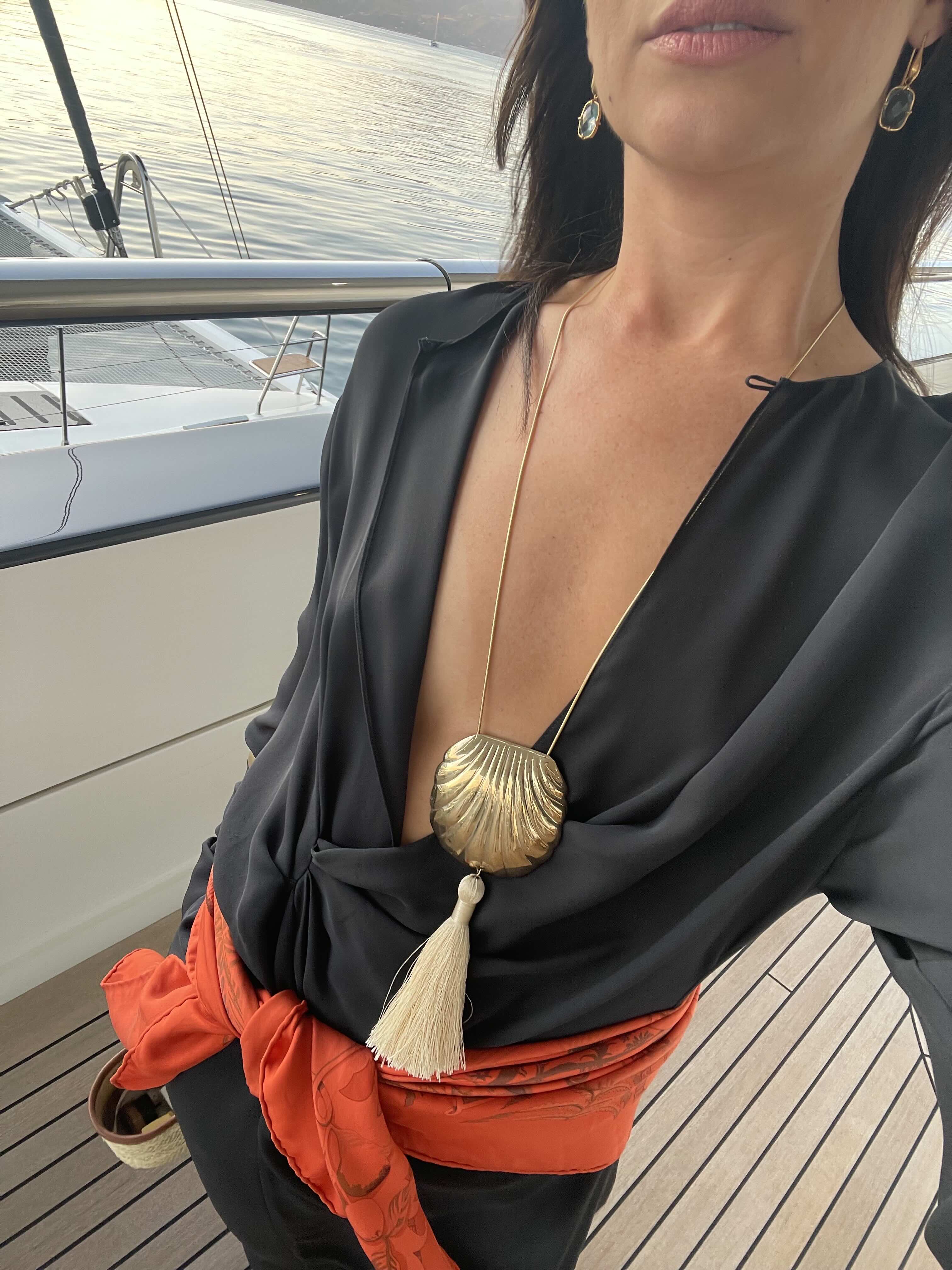 Juju Ferentinos in a black plunging dress, a gold shell pendant necklace, and orange scarf around her waist as a belt