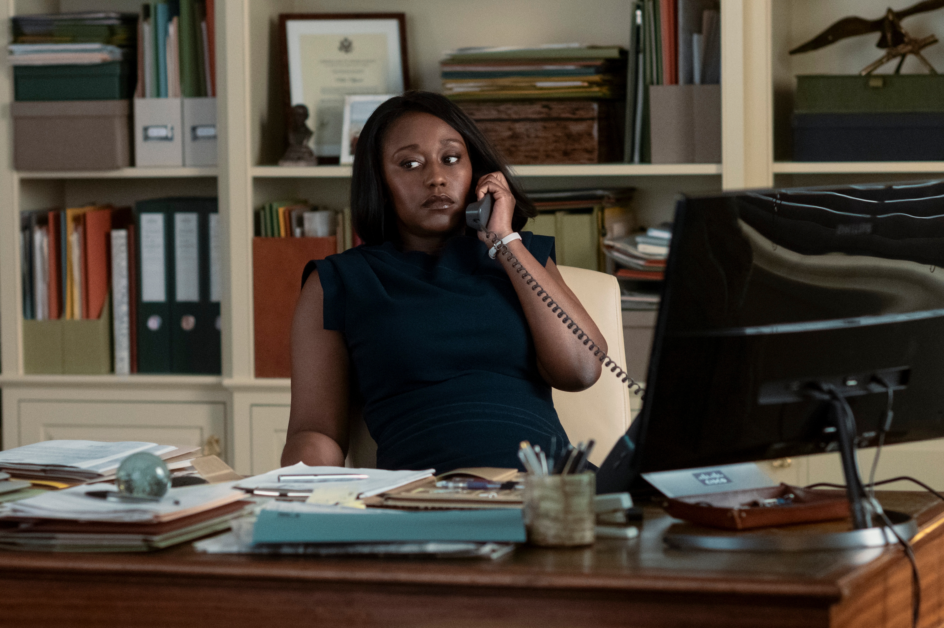 Nana Mensah as billie appiah answering a phone in an office in the diplomat